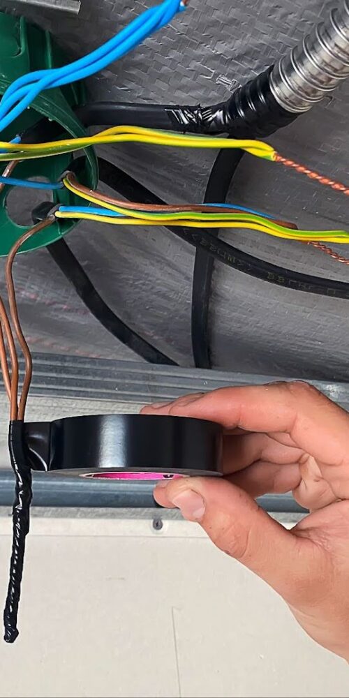 Applying black 3M Scotch Vinyl Electrical Tape Super 33+ for wire insulation inside a junction box.